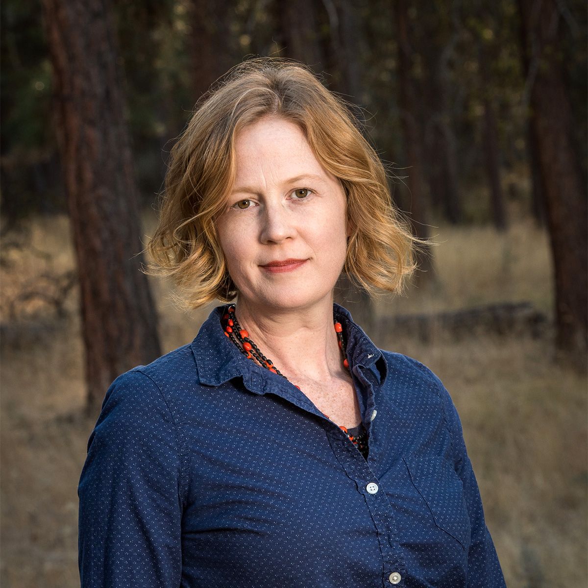 Author Emma Marris stands in front of a forest, looking at the camera.