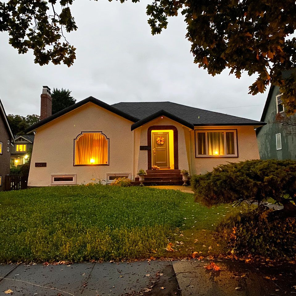 A house with the lights on, at dusk, with the bee meadow visible in the front yard