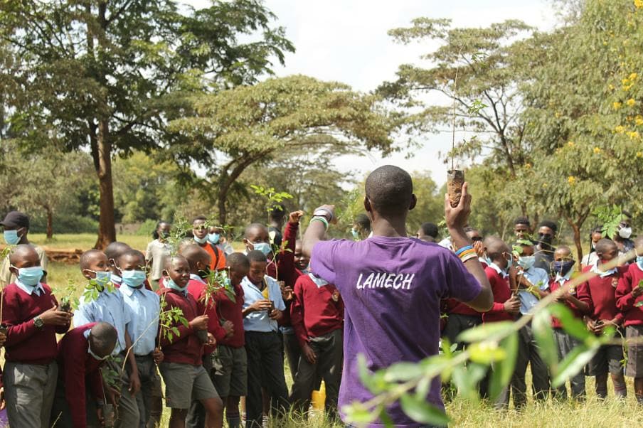 Lamech Opiyo holding a seedling and presenting to a group of schoolchildren