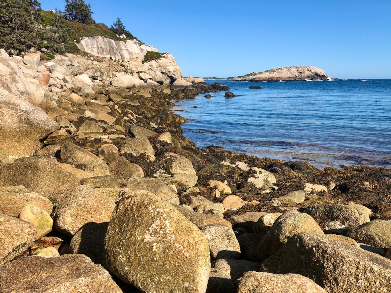 A rocky ocean bay in the sun with an island visible in the distance.