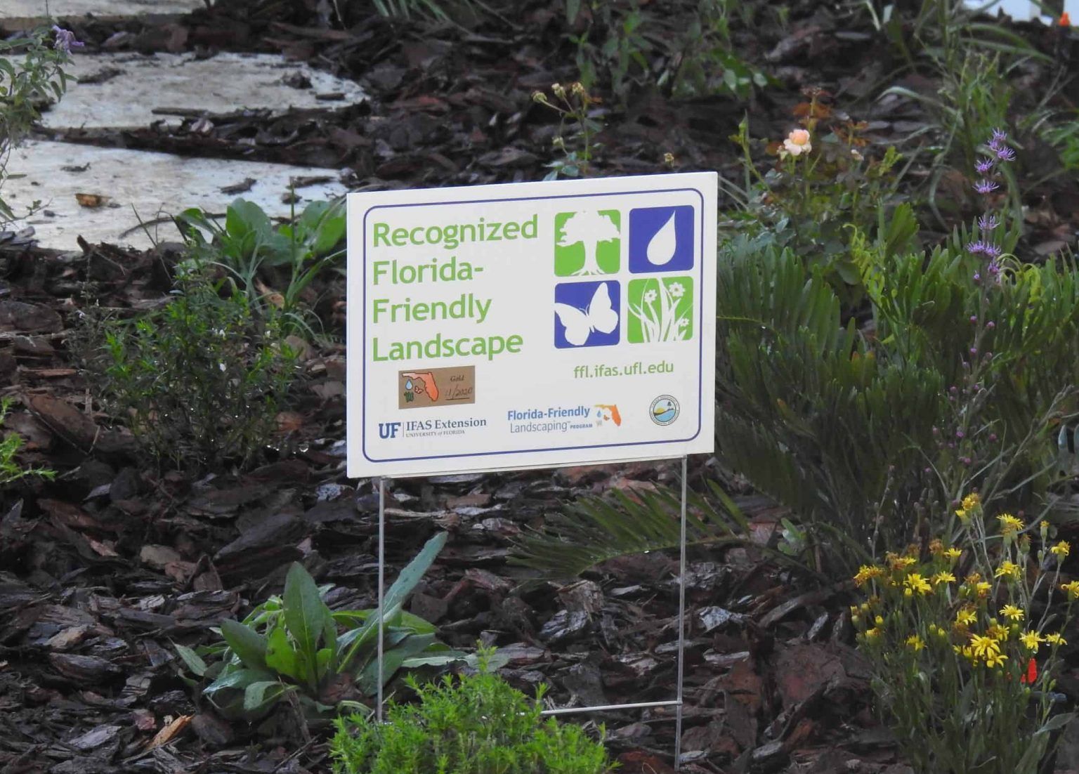 In a garden, a sign reads "Recognized Florida-Friendly Landscape"