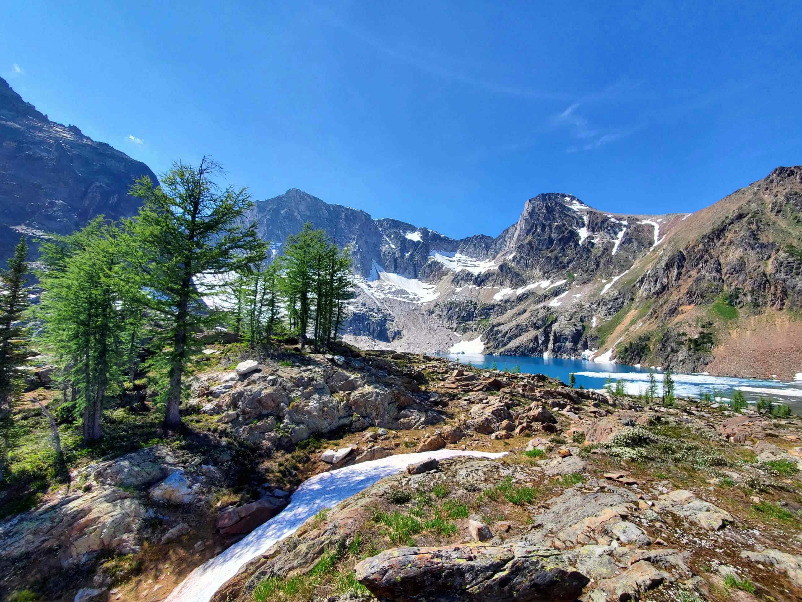 Nature scene: Rocky Mountains, trees, lake, rocks, snow, blue sky