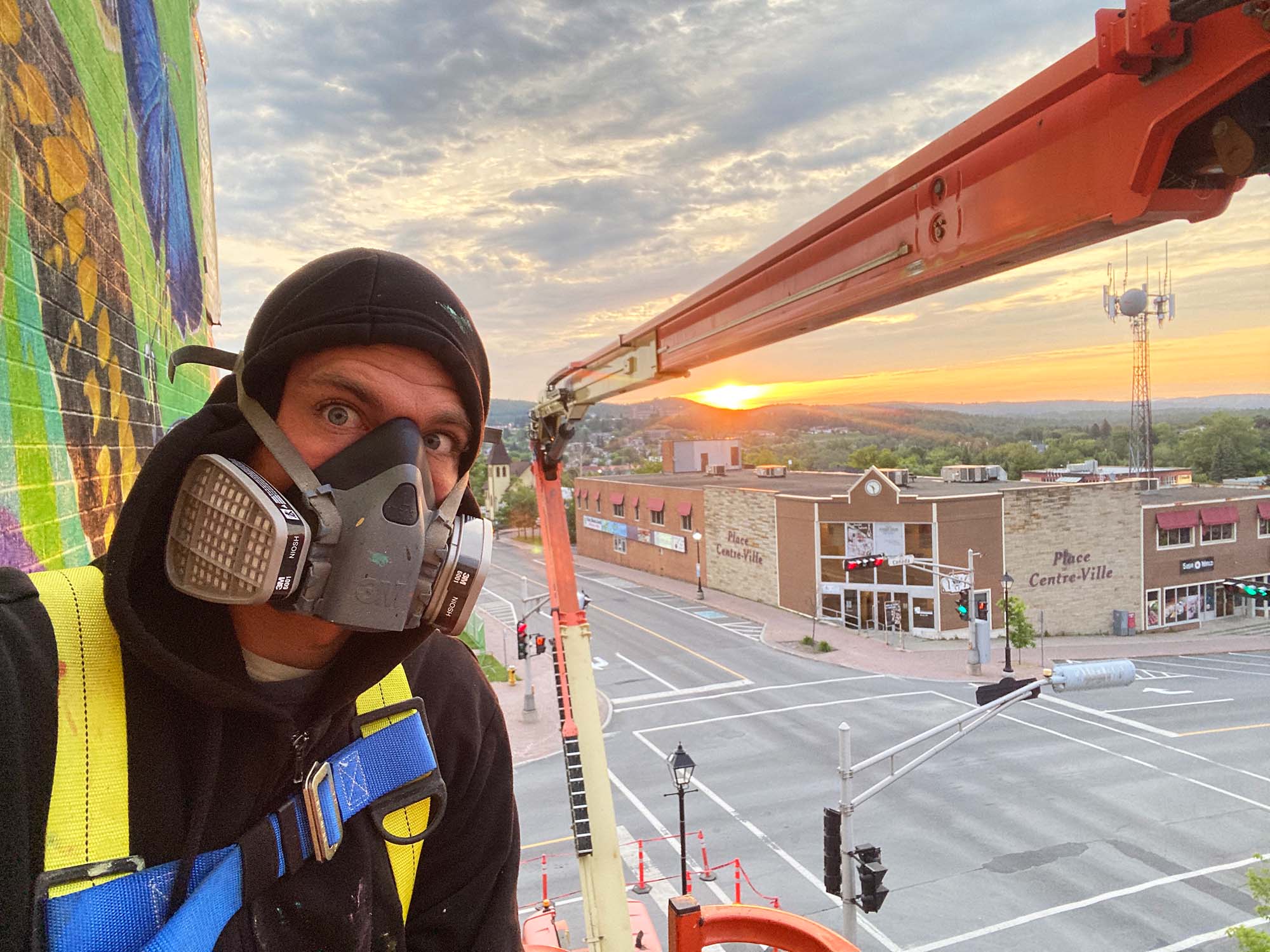 Selfie of a person wearing a respirator high above a city intersection at sunset
