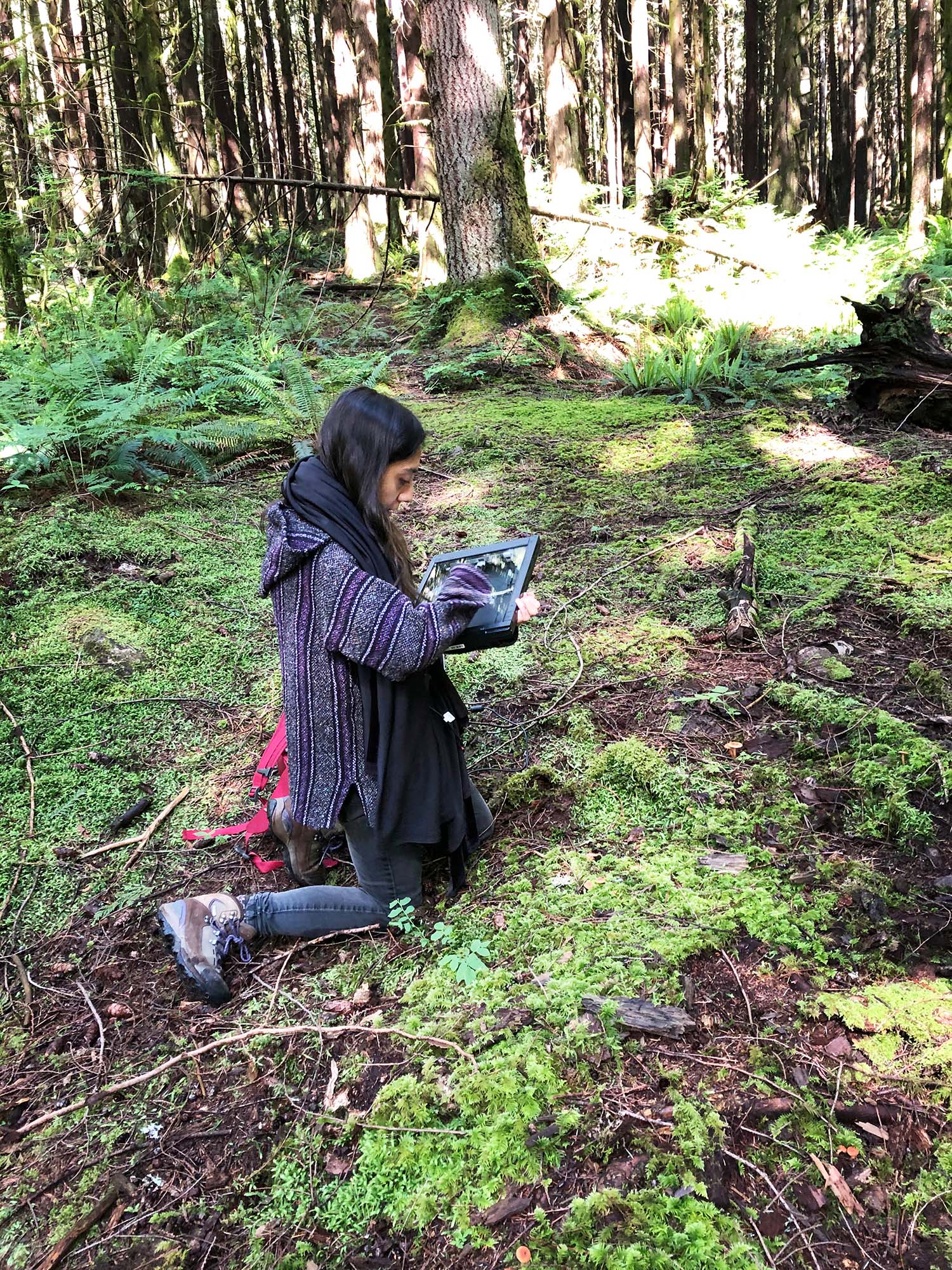 A person kneeling on the forest floor holding a portable scanner