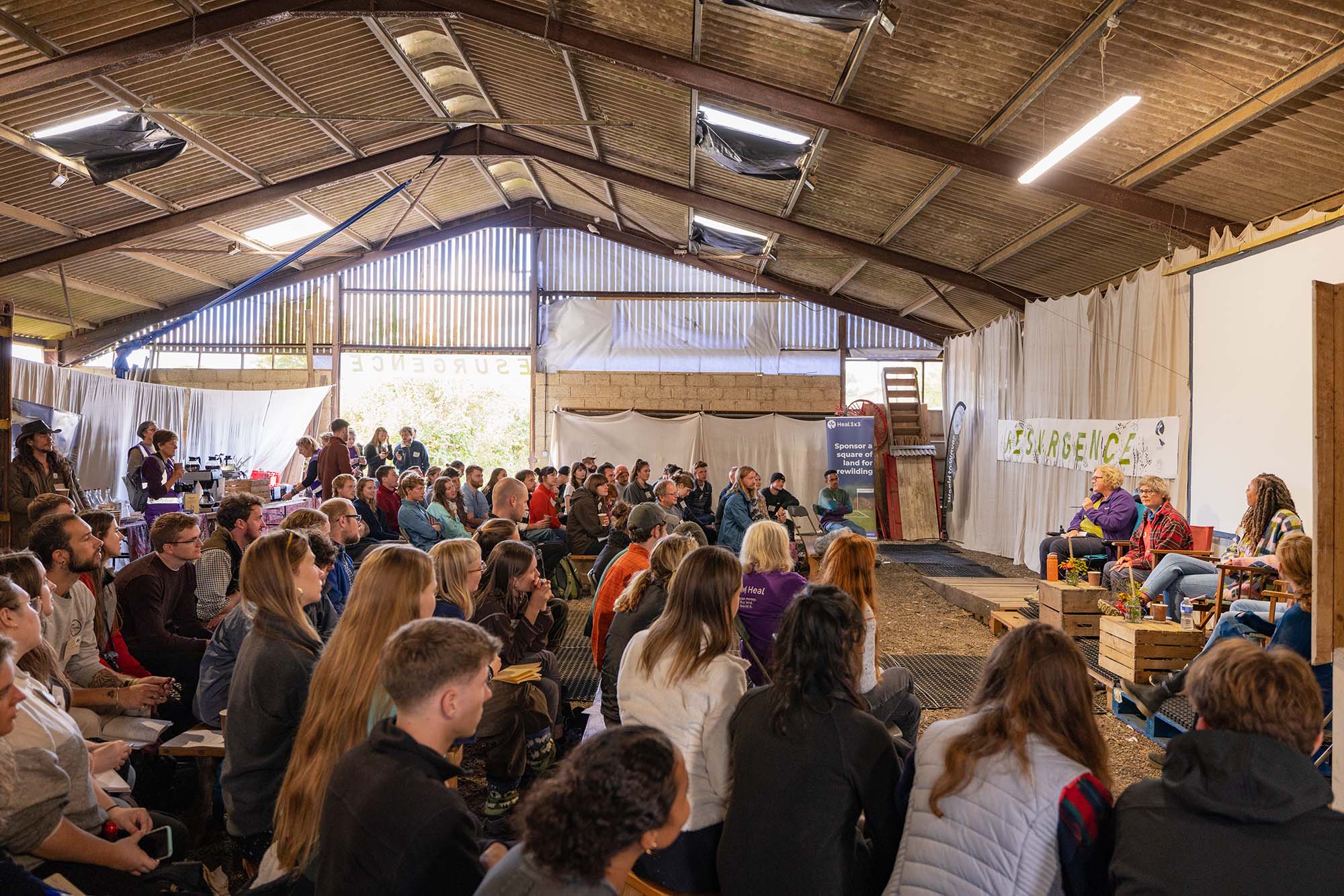 A conference inside a barn with many people watching a panel of speakers