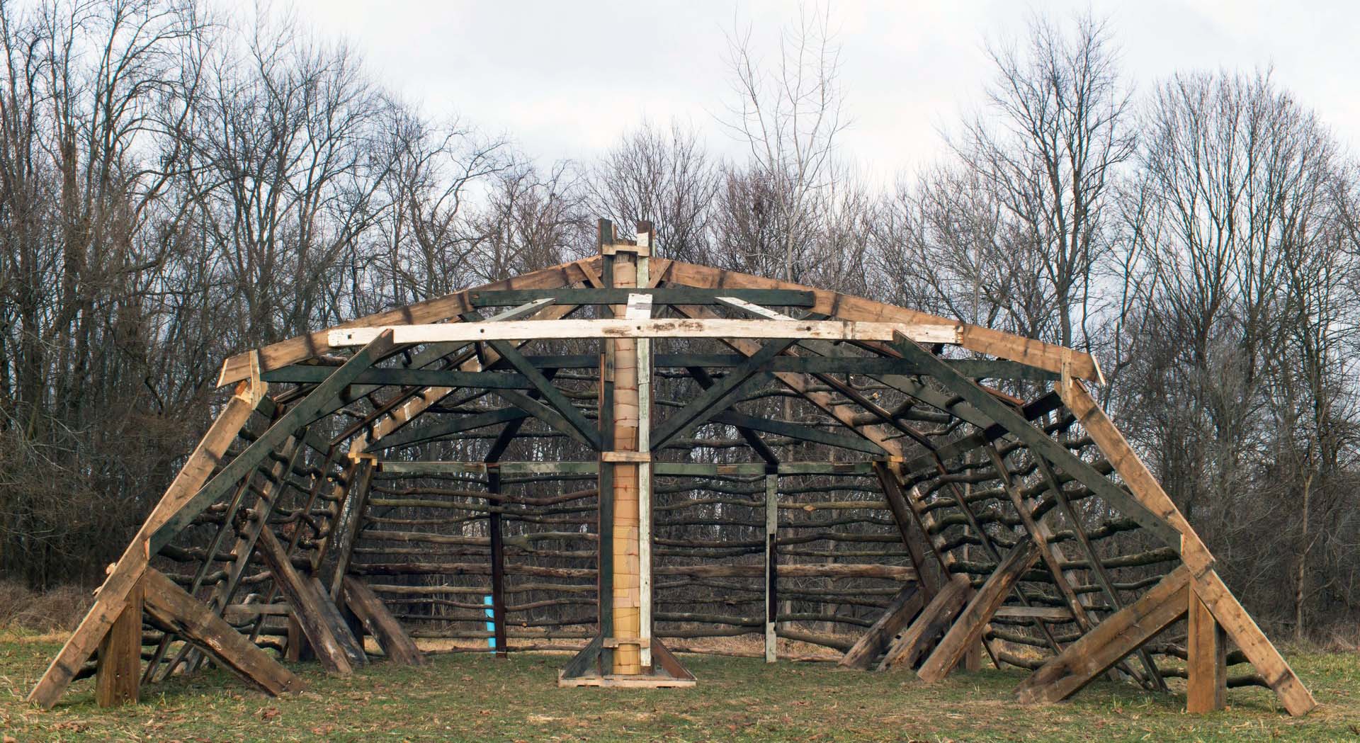 A squat wooden frame of logs and lumber in a wintry but snowless forest setting