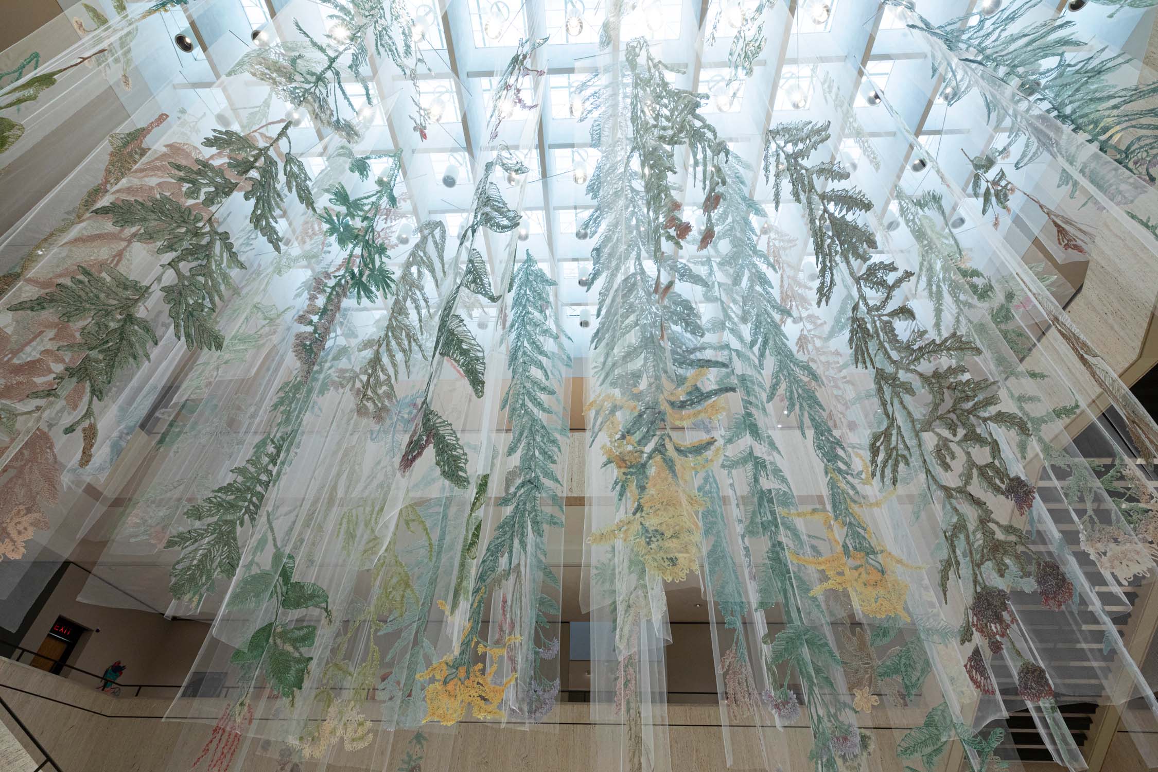 Strips of translucent fabric embroidered with plants hanging from a brightly lit ceiling