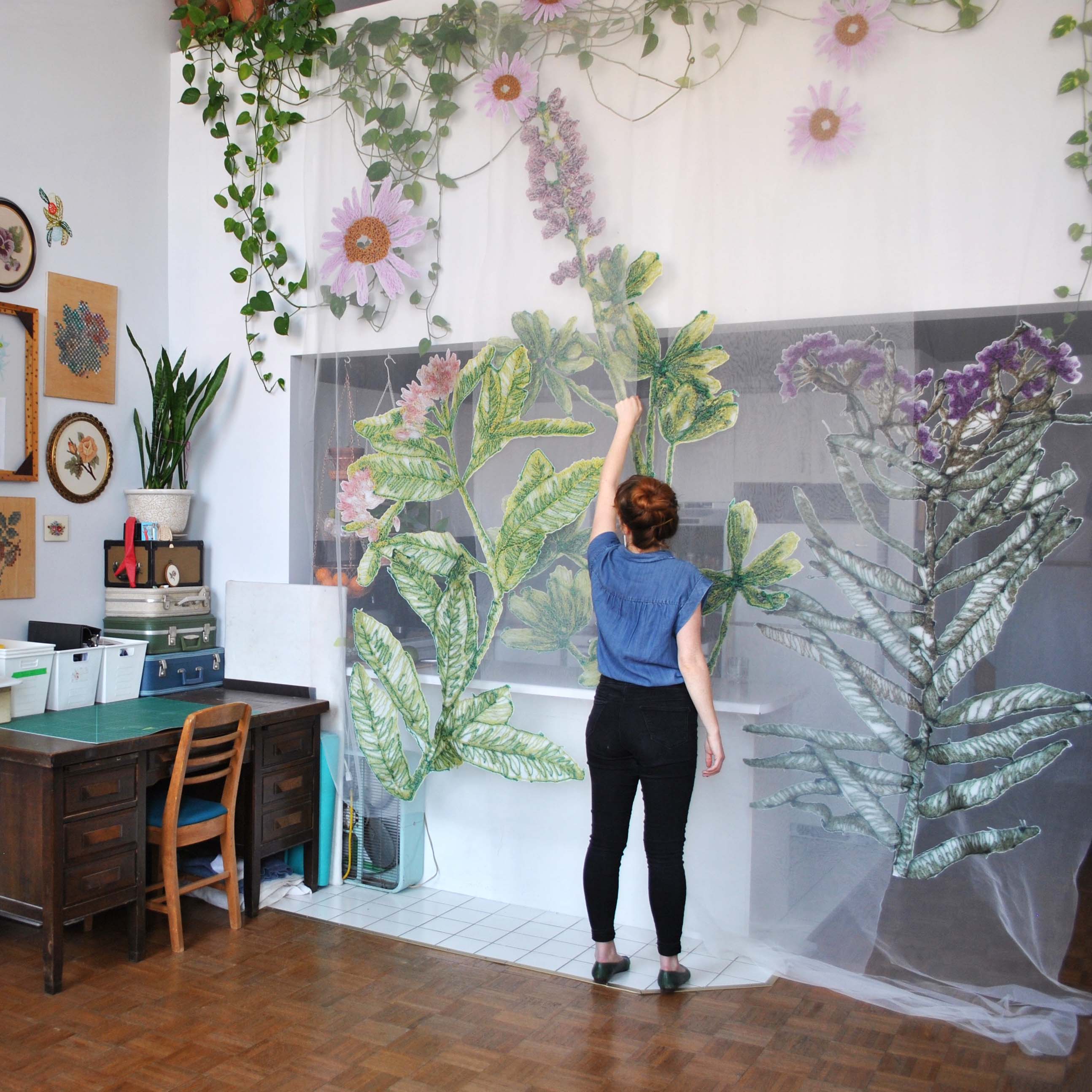 A person standing inside an apartment working on an art project involving large sketches of plants