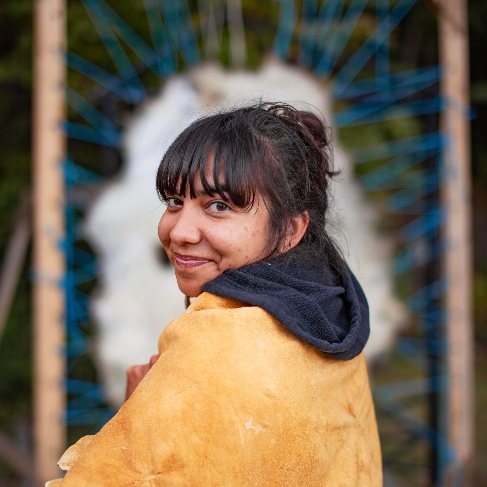 A person with leather around their shoulders, smiling at the camera