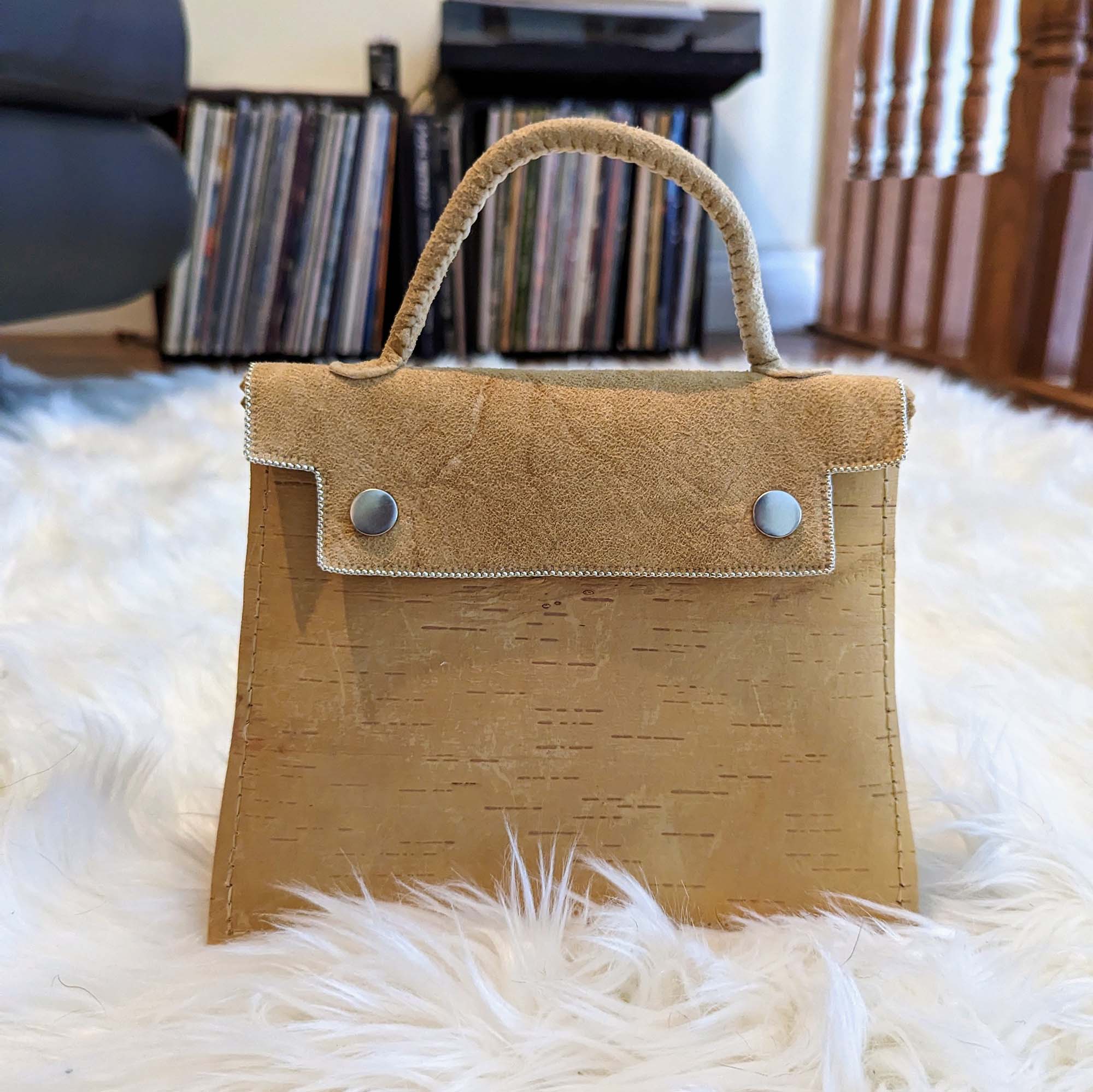 A handbag made of leather and birchbark sitting on a fluffy white rug