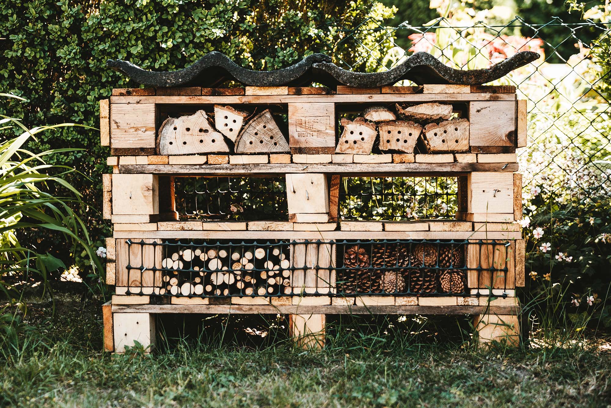 A large bee hotel with stacks of various logs, branches and pinecones