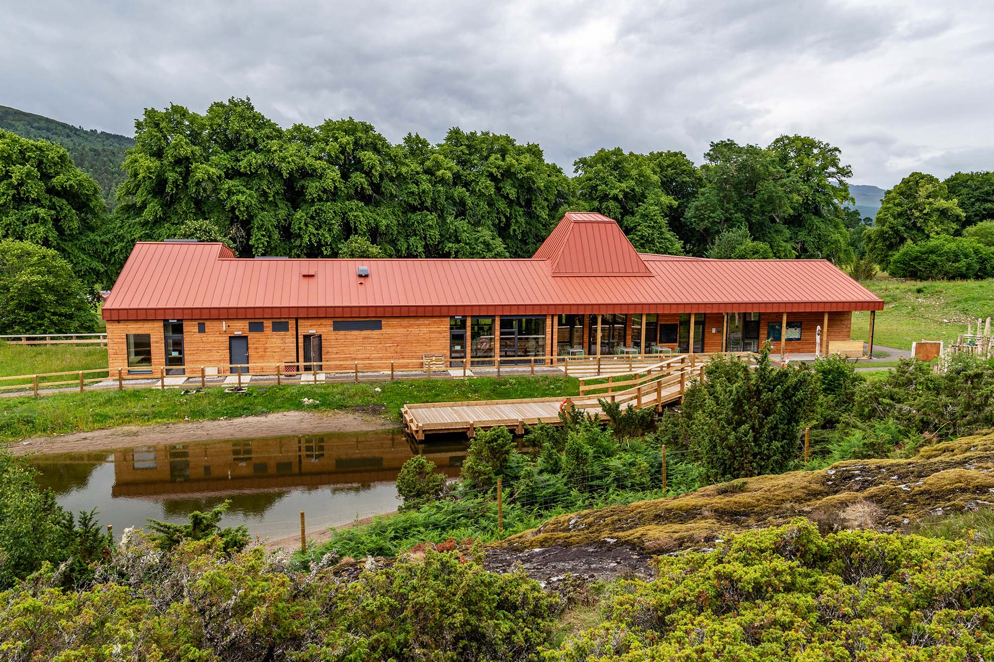 A wood-sided building with red metal roof surrounded by greenery