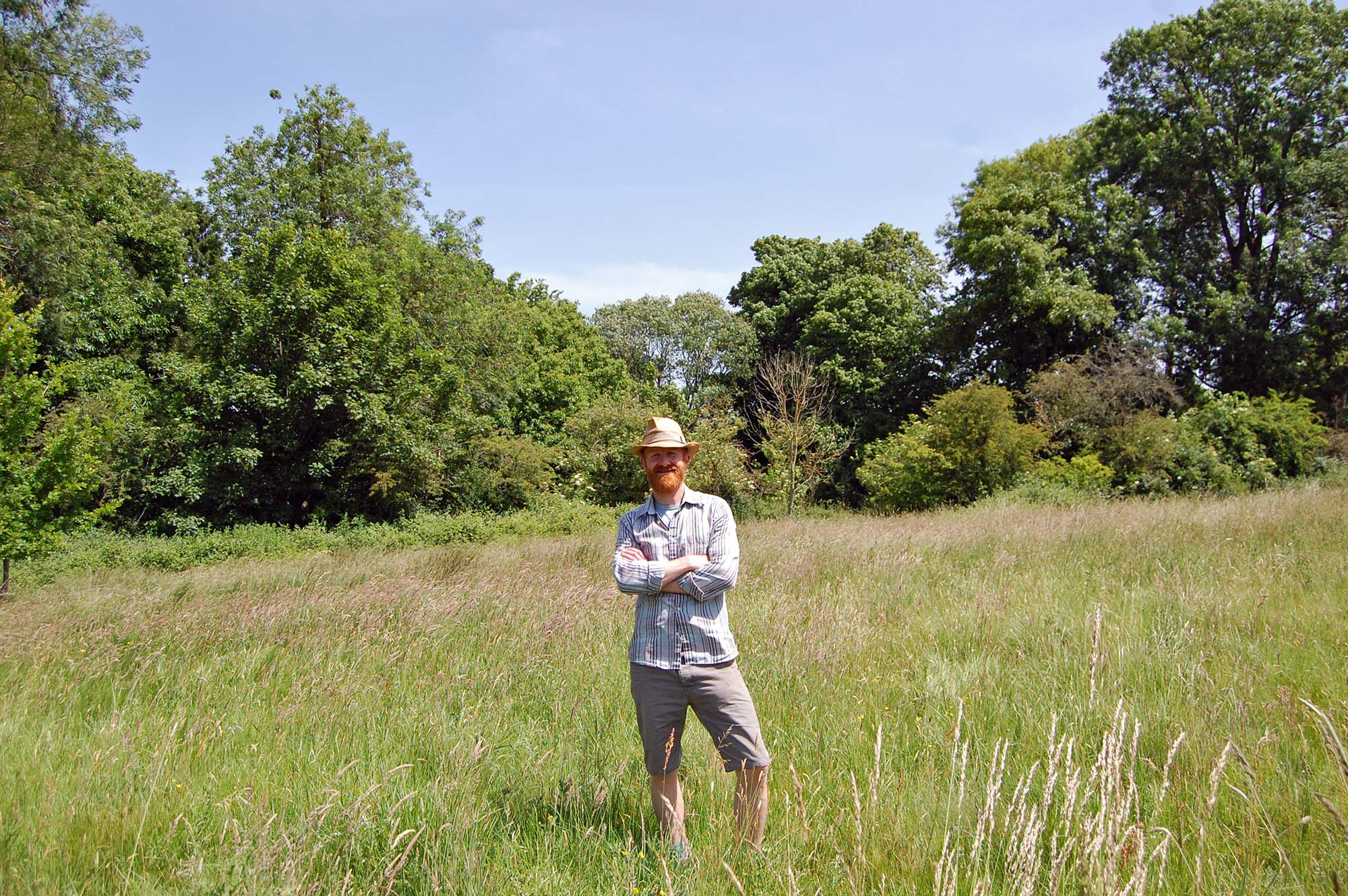 A person standing in the middle of a grassy field, with trees in the background