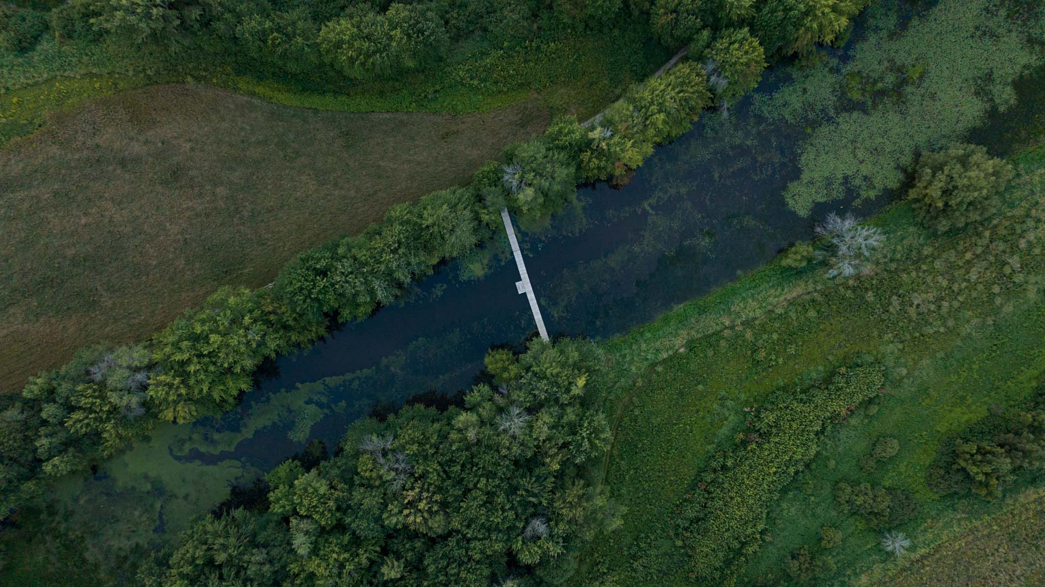 Aerial view of green land with a waterway cutting across diagonally, spanned by a bridge