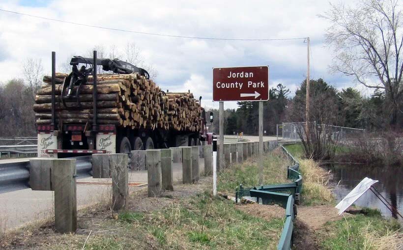 A logging truck driving a long a highway. At right, green barriers direct turtles to a tunnel.