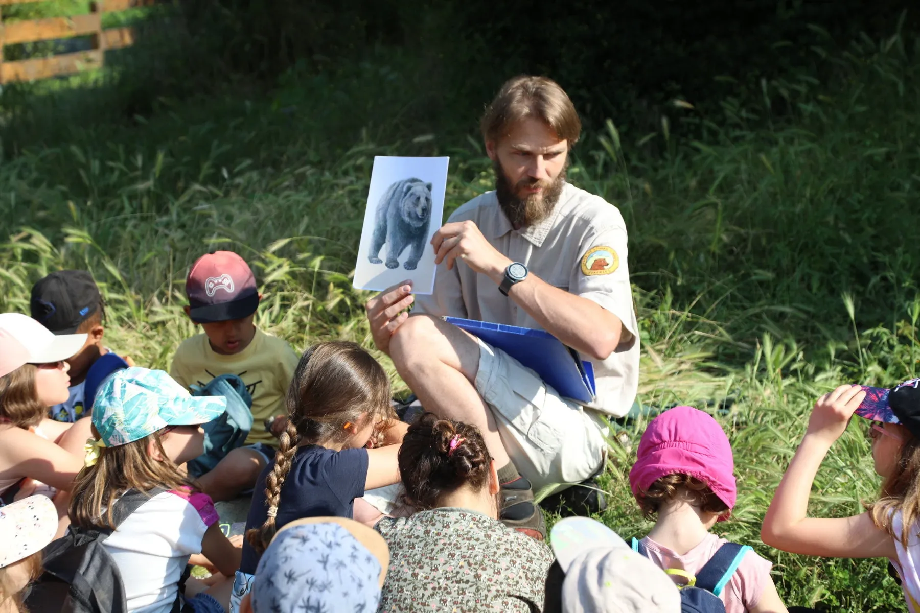 A person holding up a picture of a bear to show to a group of children, outdoors