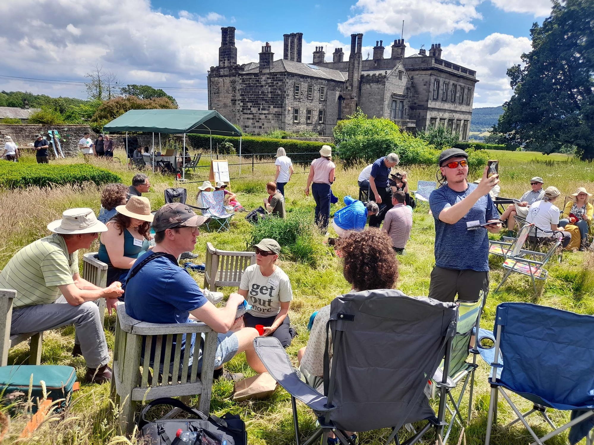 A group of people seated outdoors on a bright day, with a stone building in the background