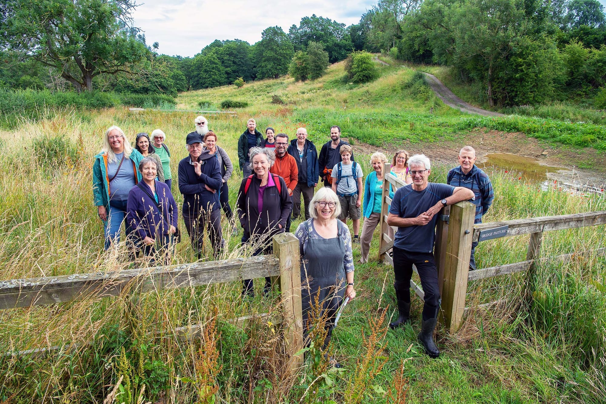 A group of people posing outdoors, at a fence opening in a green natural landscape