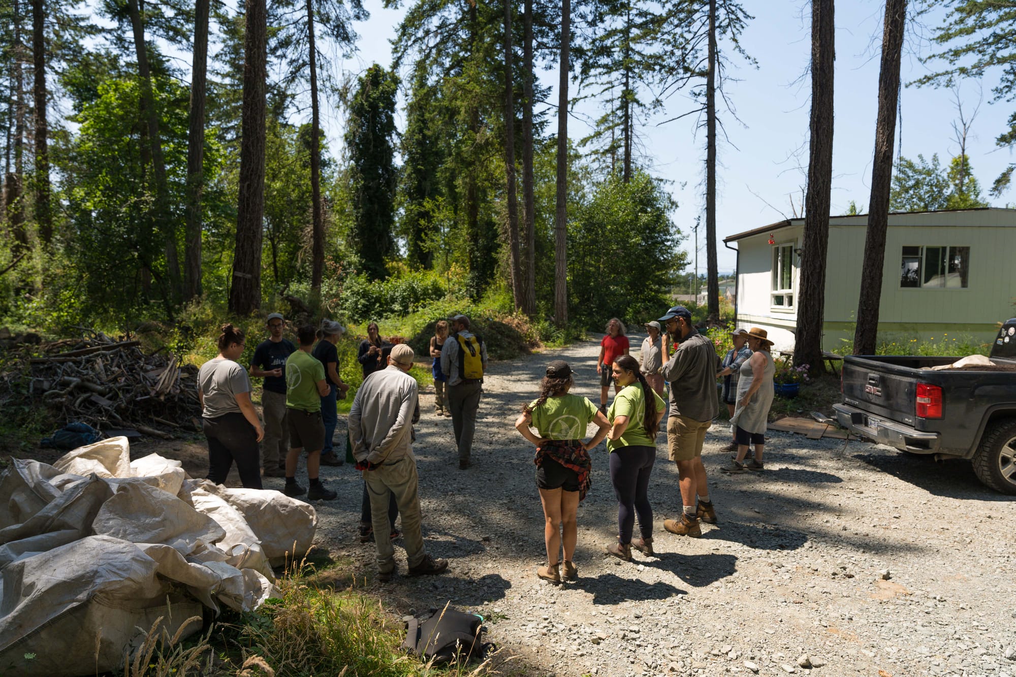 A group of people standing in a circle in a gravel parking lot next to forested land