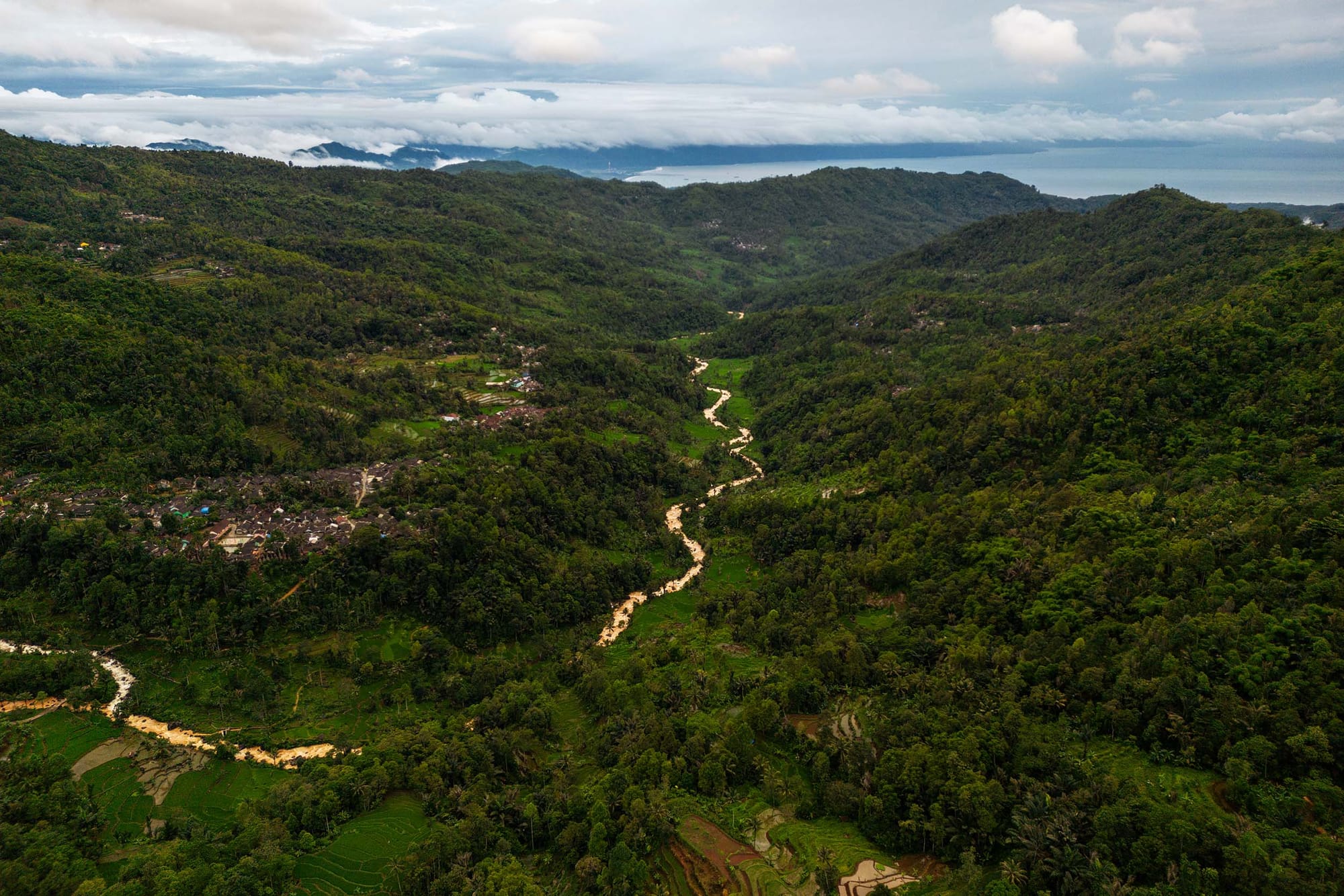 Aerial view of a road winding through a valley, with forested hills on either side and water visible beyond