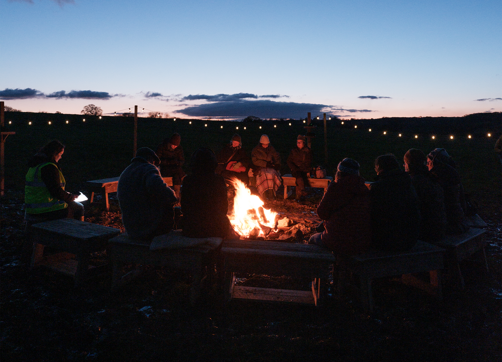 A group of people outside around a fire, at twilight