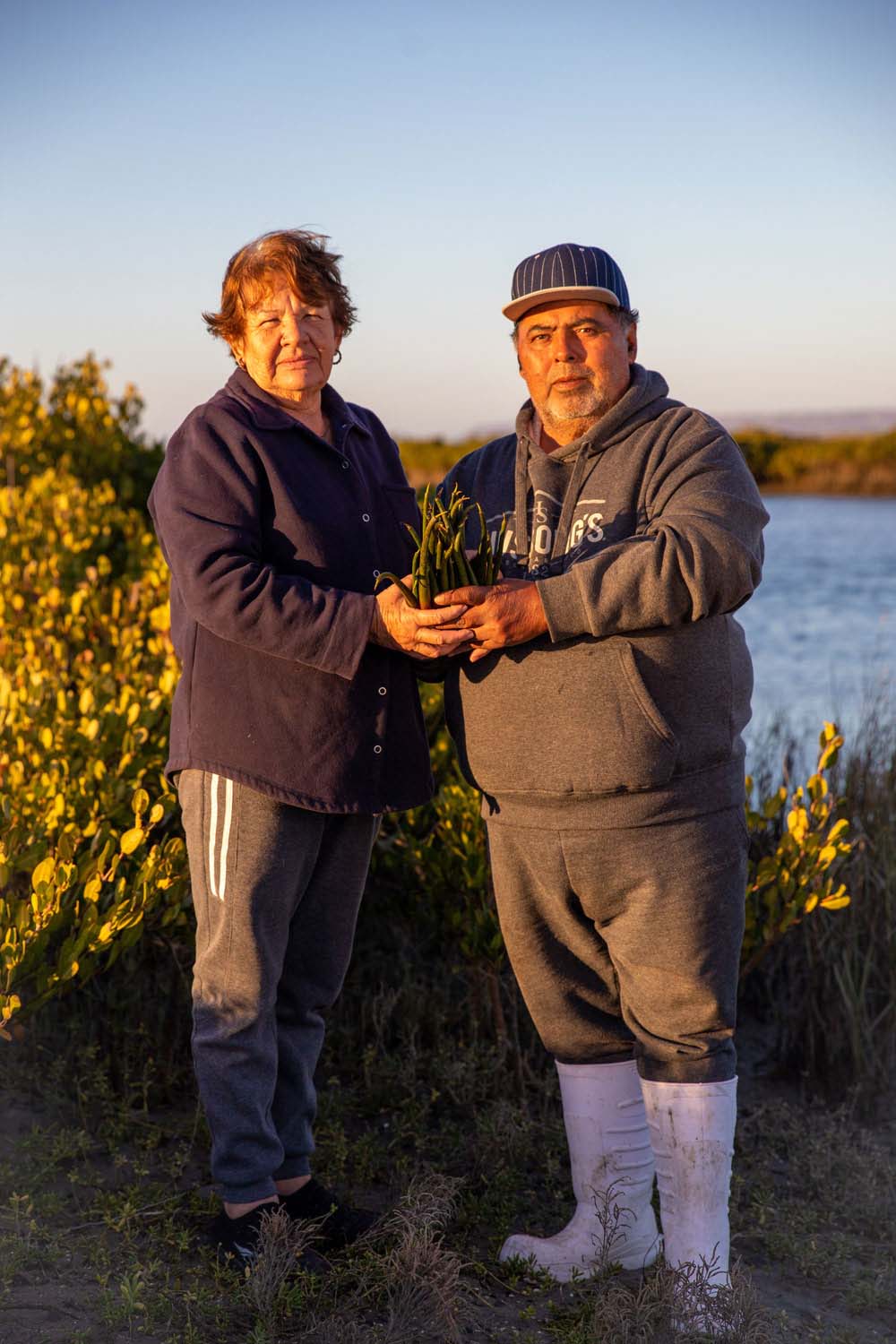 Two people posing for the camera, outdoors, holding mangrove propagules