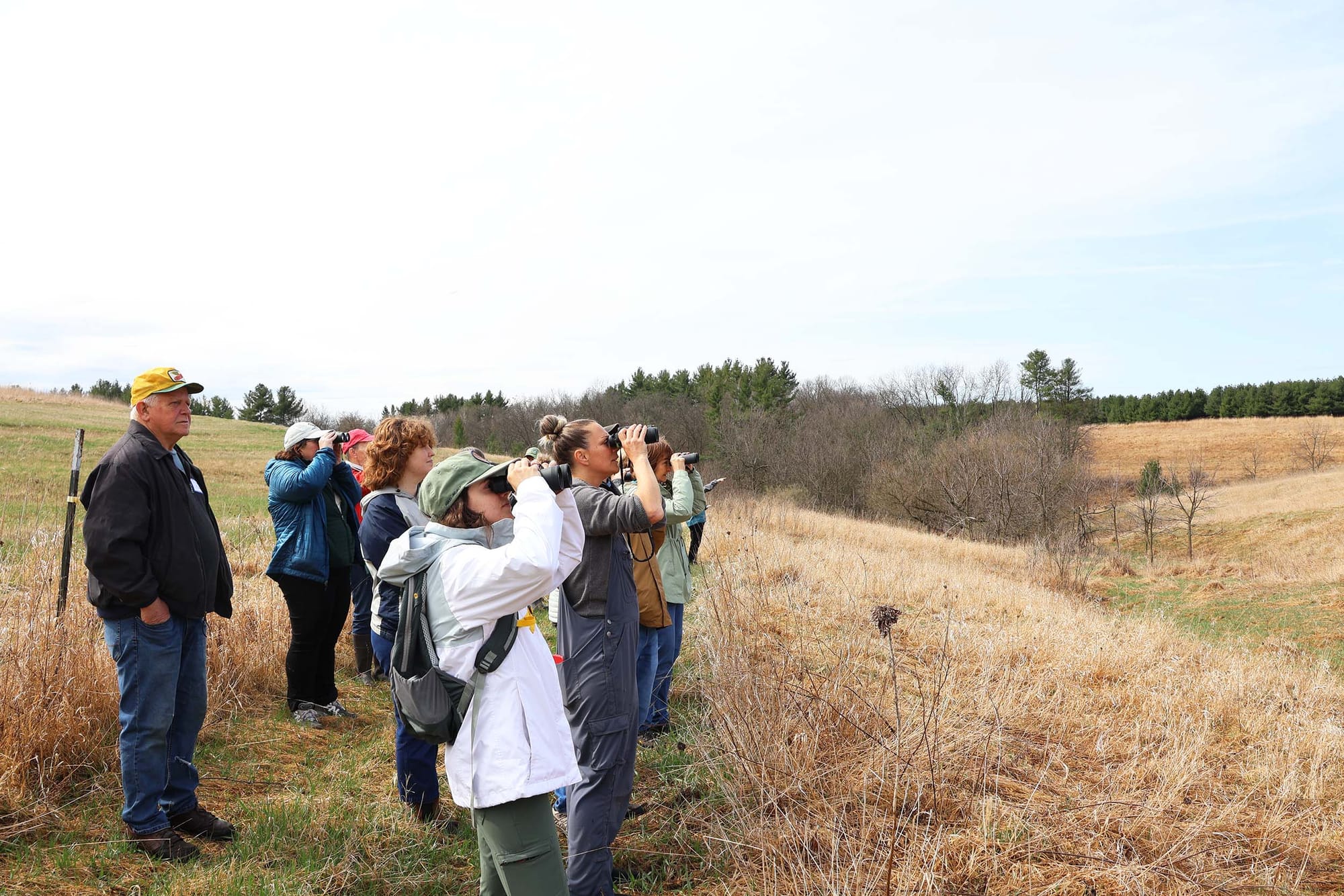 A group of people standing outside looking to the right of frame with binoculars