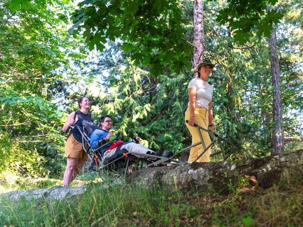 People, one using a wheelchair, smiling while going along an outdoor trail