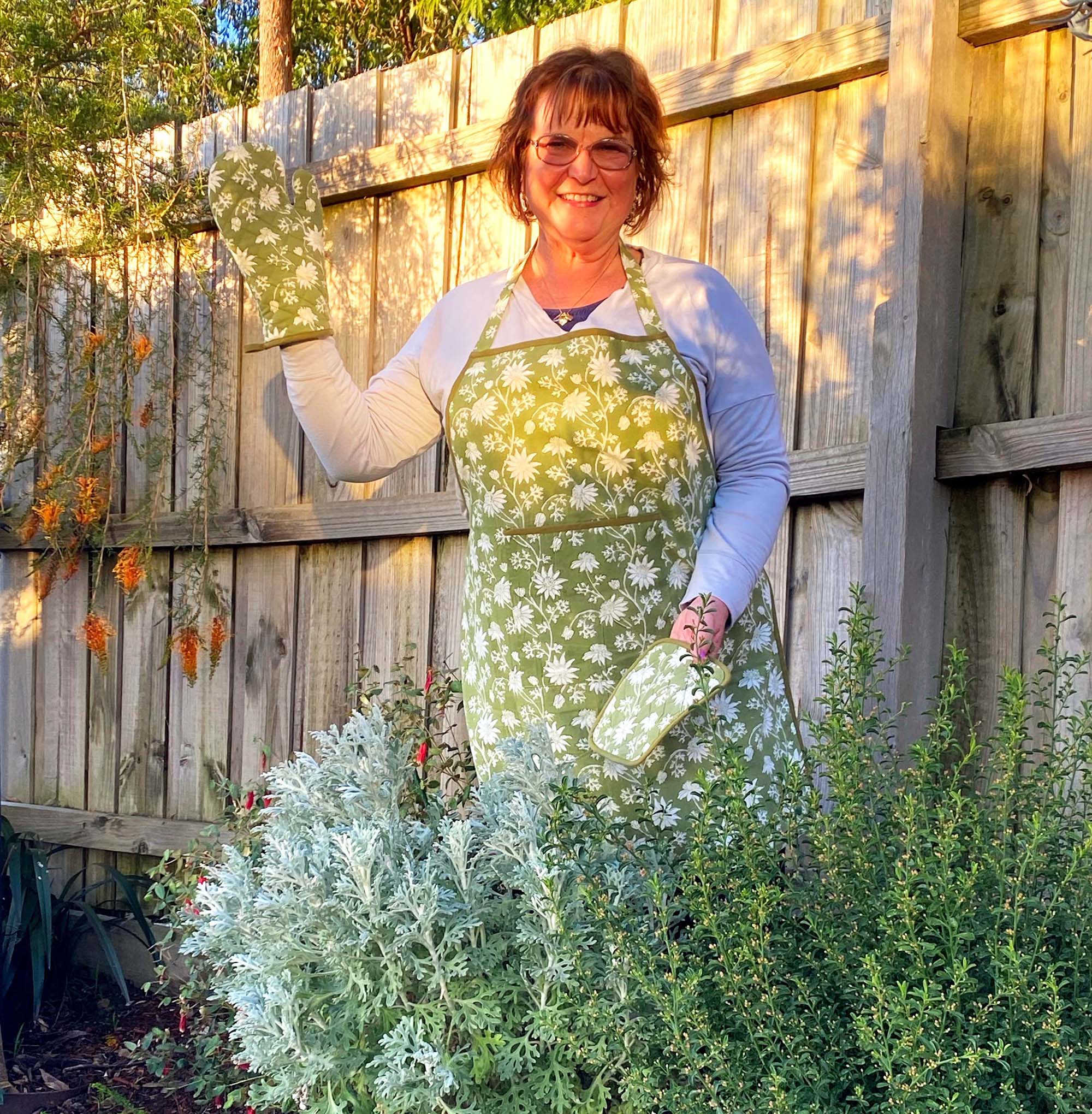 A person in a garden in front of a fence, posing and smiling for the camera