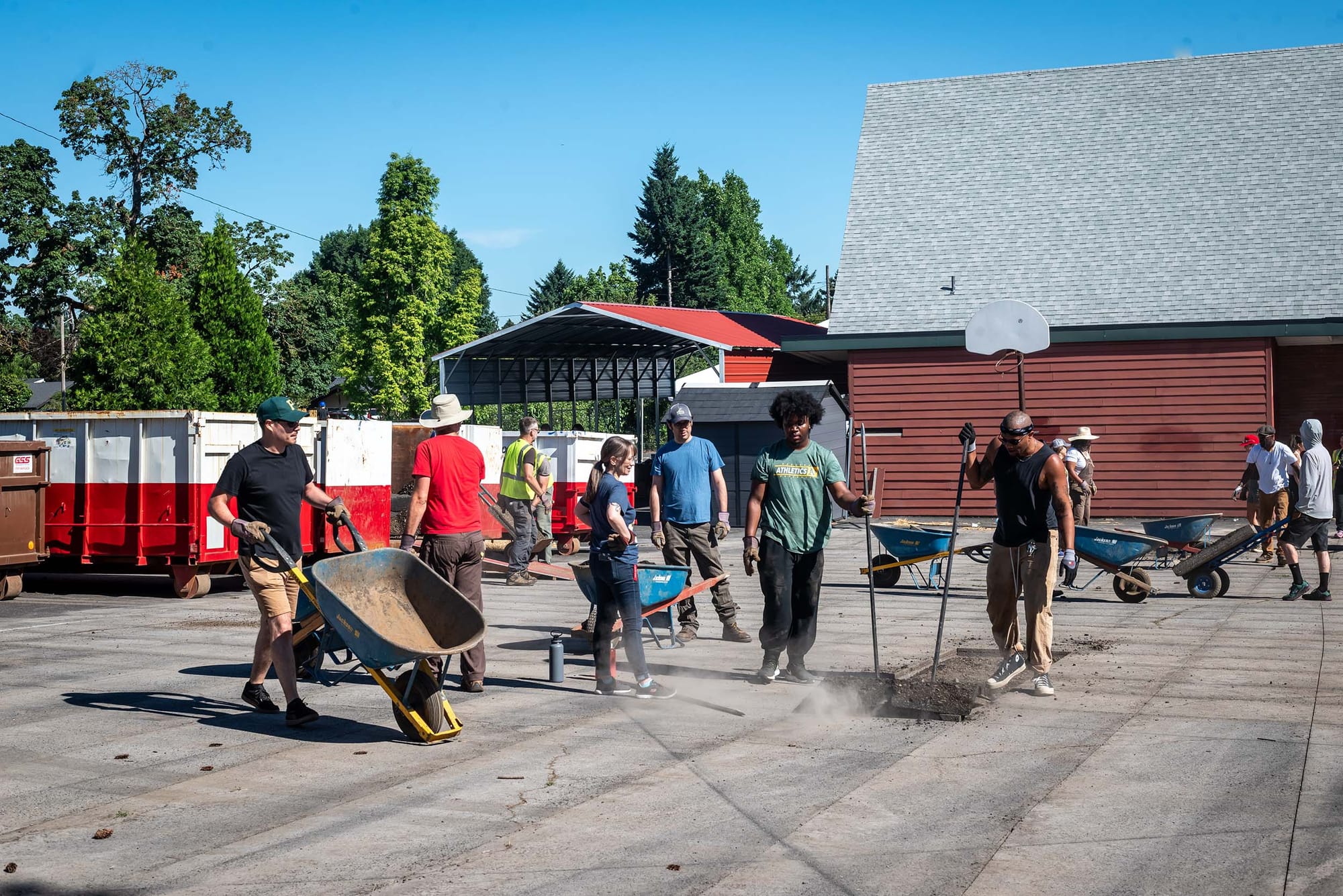 People outdoors removing pavement and moving wheelbarrows