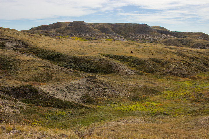 Two people walking through a rolling landscape at Grasslands National Park in Saskatchewan, Canada.