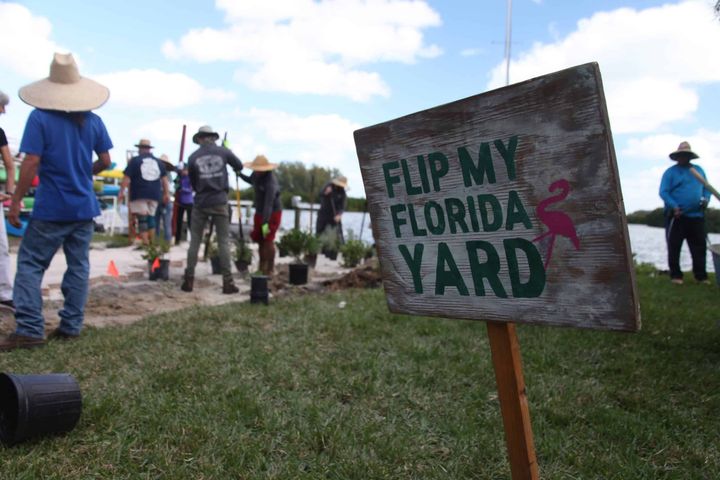 A sign reading "Flip my Florida yard" in front of a crew of gardeners in hats