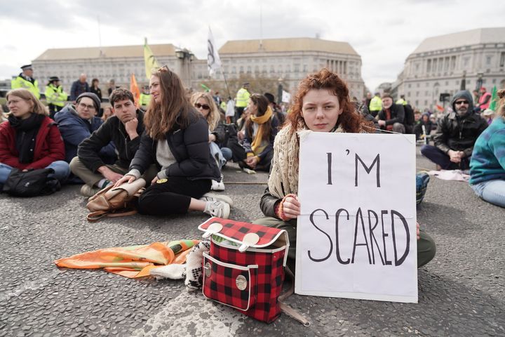 A group of protesters sitting in a city street. One woman holds a sign reading "I'm scared"