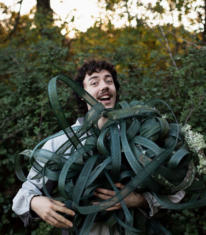 A person holding a large bundle of ribbons of green mesh fencing