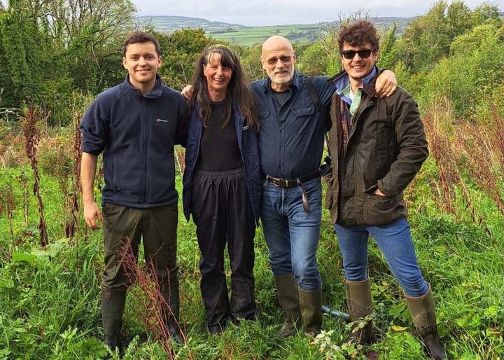 Four people standing together in a field, smiling, with rolling hills in the background