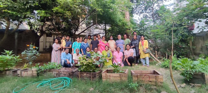 A group of people posing in a garden outdoors, surrounded by green