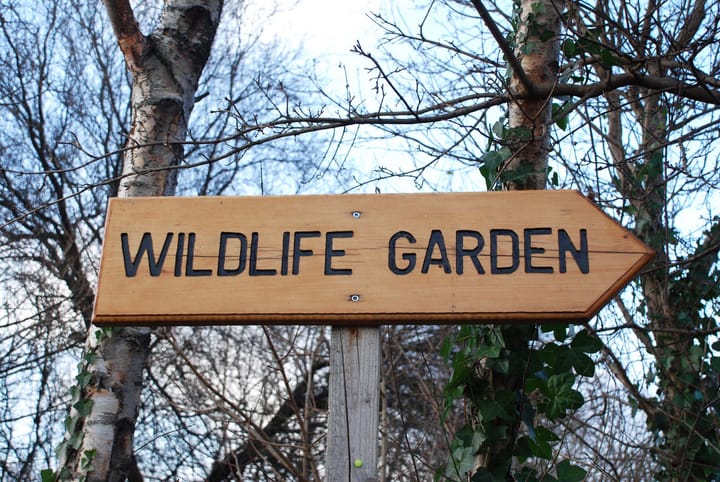 A sign in a forest that reads "wildlife garden"