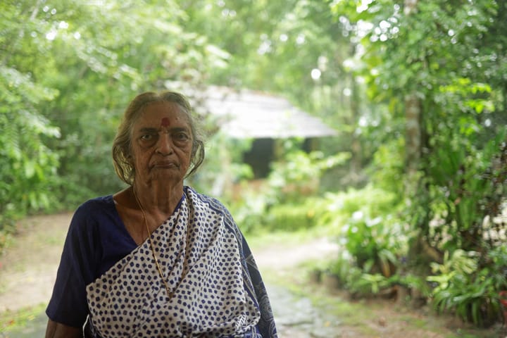 A person looking at the camera while standing outdoors, surrounded by greenery