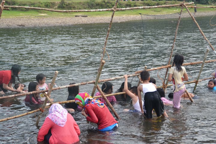 A group of people in a river positioned around a bamboo and net structure