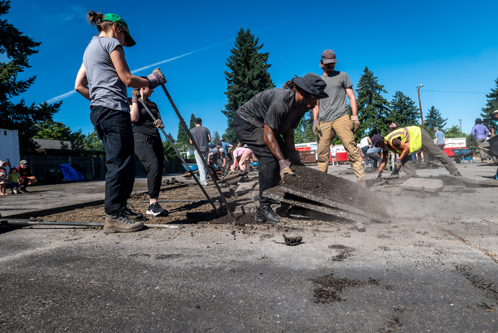 People outdoors removing pavement from a parking lot, with bright blue sky in the background